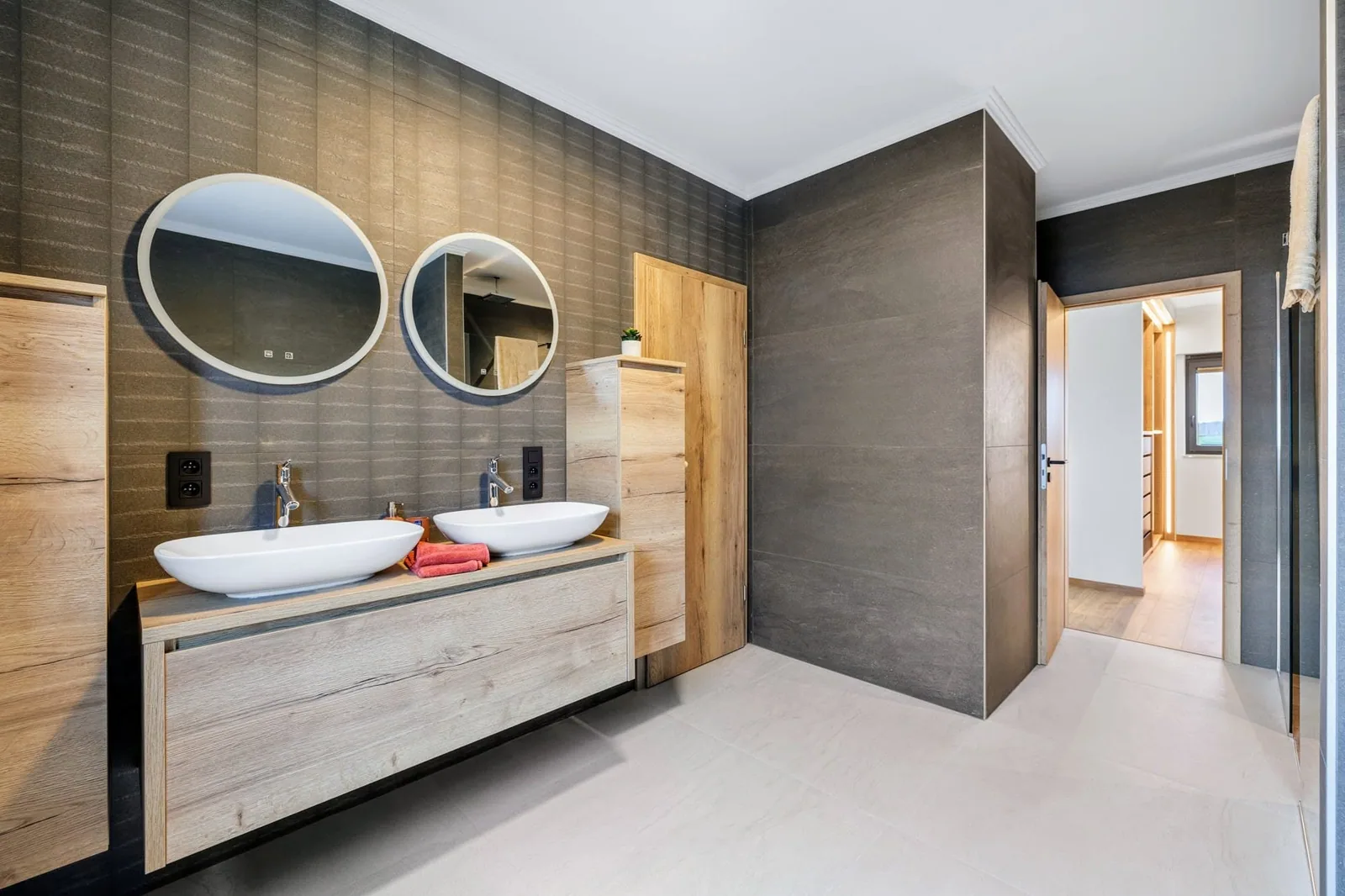 Salle de bains terminée : mur en grande dalle effet pierre, double vasque et miroirs ronds