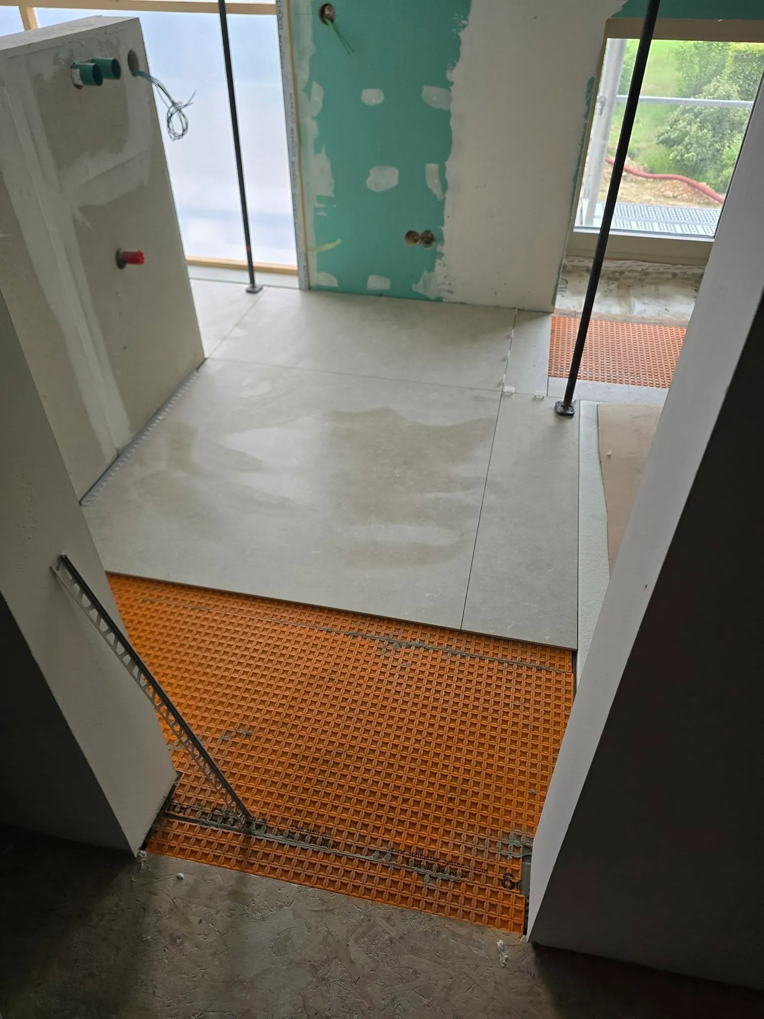 Chantier en cours : la natte de désolidarisation Schlüter Ditra orange, à demi recouverte par les grandes dalles déjà posées